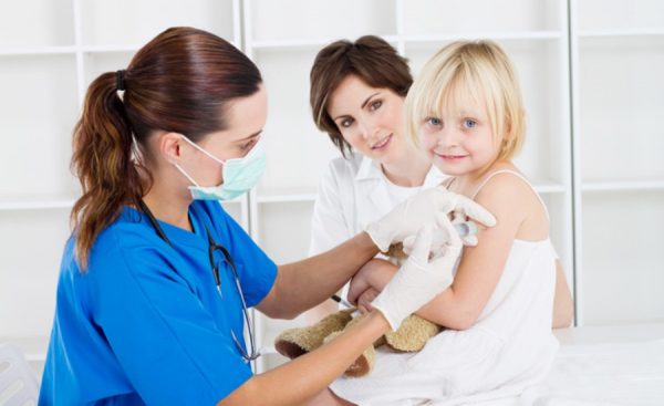 A doctor and two women are examining a child.